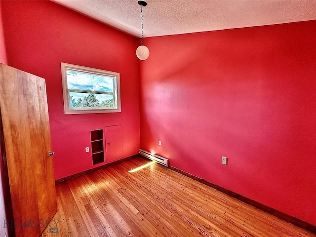 empty room featuring a textured ceiling, hardwood / wood-style flooring, and baseboard heating