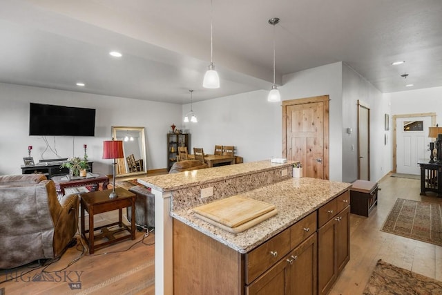 kitchen with a kitchen island, light stone counters, light wood-type flooring, and hanging light fixtures