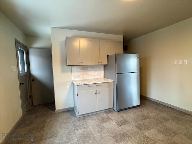 kitchen with decorative backsplash, light stone counters, and stainless steel refrigerator