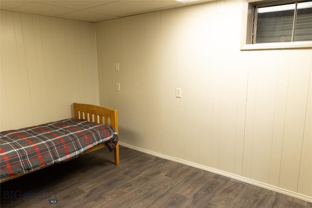 bedroom with dark hardwood / wood-style floors, a drop ceiling, and wood walls