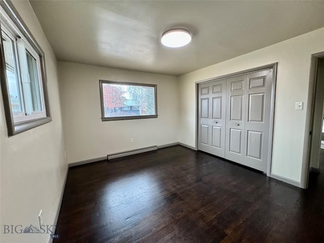 unfurnished bedroom with dark wood-type flooring, baseboard heating, and a closet