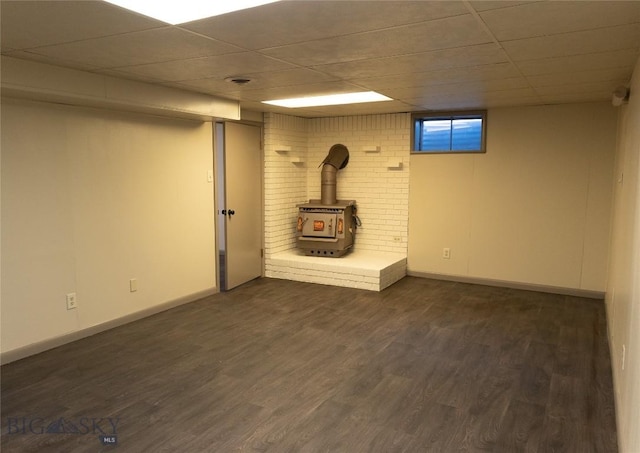 basement featuring a wood stove, a paneled ceiling, and dark hardwood / wood-style flooring