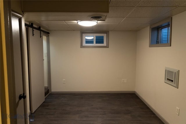 basement featuring a barn door, dark hardwood / wood-style floors, and a paneled ceiling