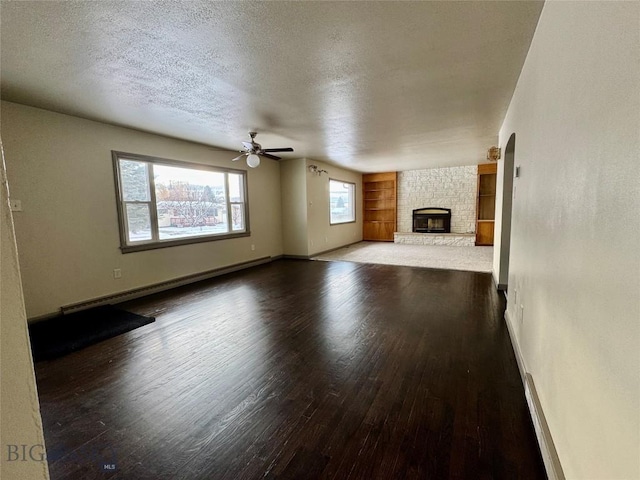 unfurnished living room with a stone fireplace, ceiling fan, a textured ceiling, a baseboard radiator, and wood-type flooring