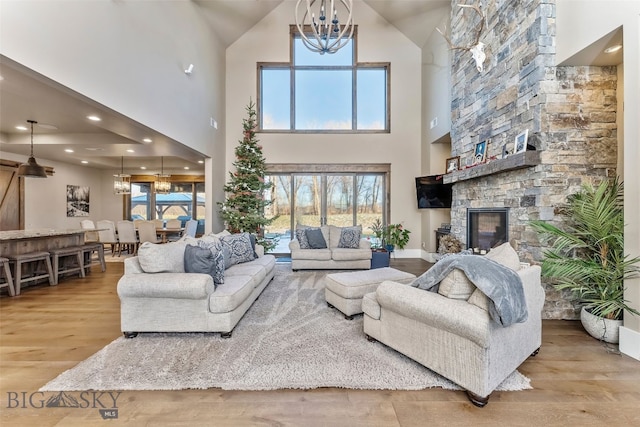 living room featuring a fireplace, light hardwood / wood-style flooring, high vaulted ceiling, and an inviting chandelier