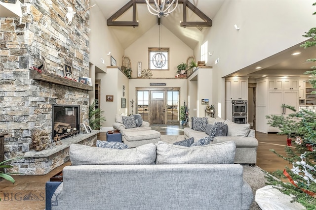 living room with a chandelier, hardwood / wood-style flooring, high vaulted ceiling, and a stone fireplace