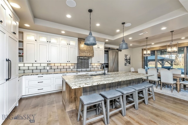 kitchen with a center island with sink, a barn door, white cabinetry, and a tray ceiling