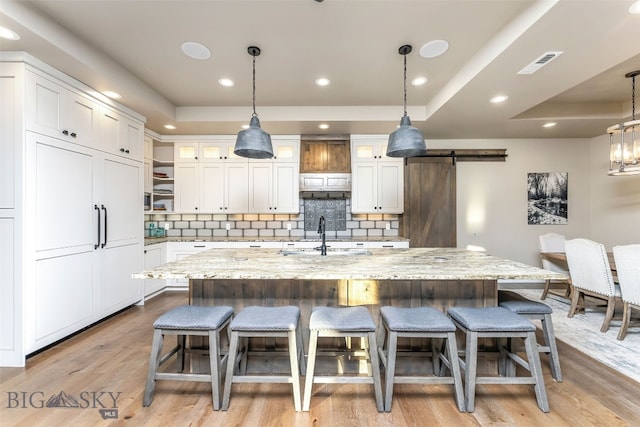 kitchen featuring sink, a barn door, light wood-type flooring, tasteful backsplash, and a large island