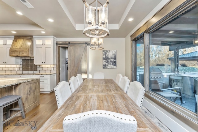 dining room with a barn door, an inviting chandelier, light hardwood / wood-style flooring, and a tray ceiling