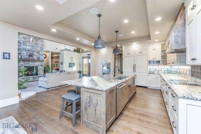 kitchen featuring light stone countertops, a large island with sink, built in appliances, pendant lighting, and white cabinets