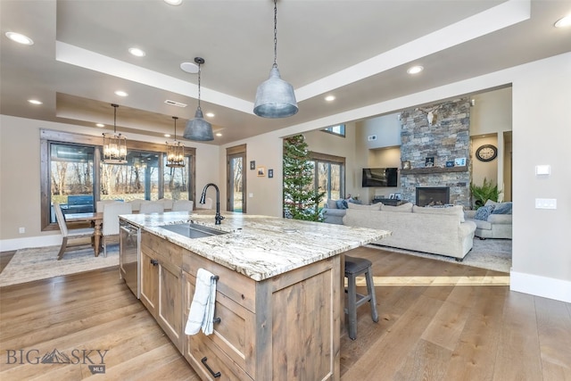 kitchen with light wood-type flooring, a tray ceiling, a spacious island, sink, and hanging light fixtures