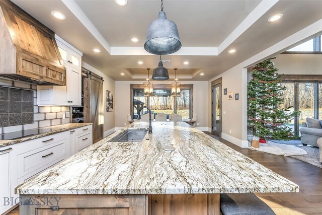 4807 Jordan Spur Rd, Bozeman, MT 59715 - kitchen with a tray ceiling, a barn door, tasteful backsplash, white cabinetry, and custom exhaust hood