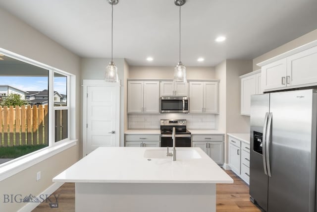 kitchen with backsplash, white cabinets, hanging light fixtures, appliances with stainless steel finishes, and light hardwood / wood-style floors