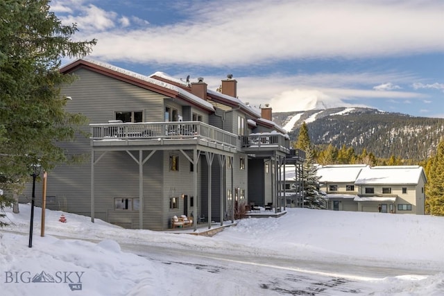 snow covered back of property with a deck with mountain view