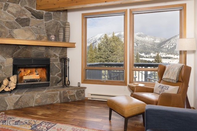 sitting room with a mountain view, hardwood / wood-style floors, a stone fireplace, and a baseboard heating unit