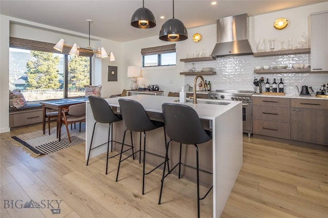 kitchen with pendant lighting, stainless steel stove, light hardwood / wood-style flooring, and wall chimney range hood