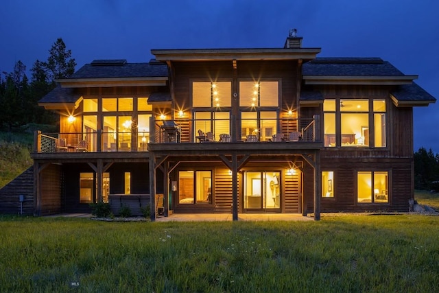 13 Middle Rider, Big Sky, MT 59716 - back of house at night with a yard, a chimney, a balcony, and a patio area