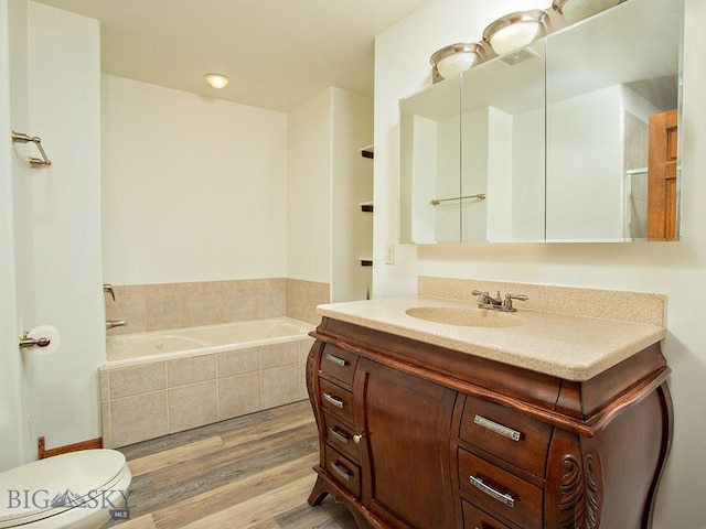 bathroom featuring tiled bath, vanity, wood-type flooring, and toilet