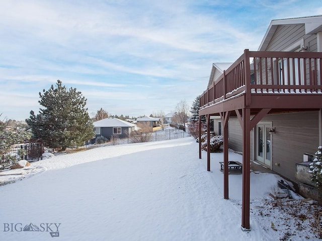 yard layered in snow with a wooden deck and french doors