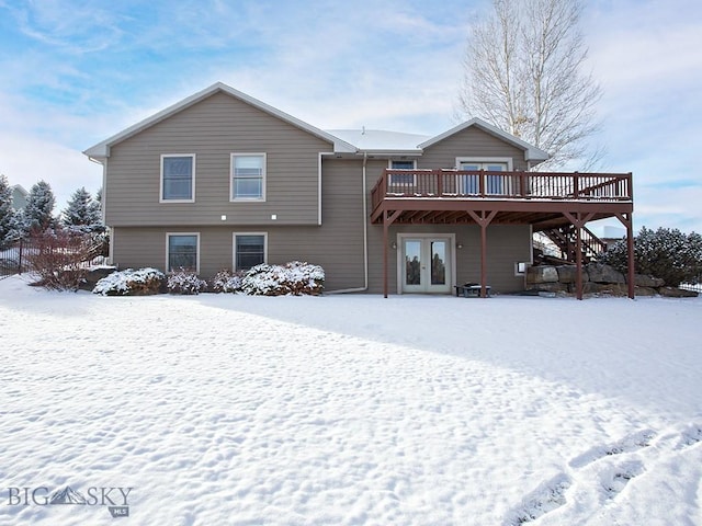 snow covered back of property with french doors and a deck