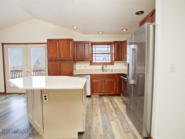 kitchen featuring appliances with stainless steel finishes, vaulted ceiling, sink, a center island, and light hardwood / wood-style floors