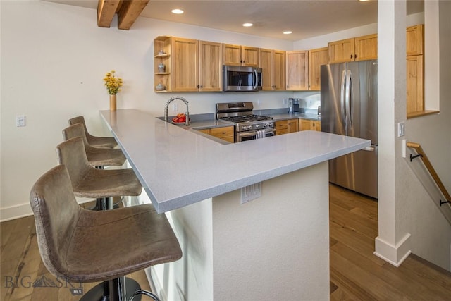 kitchen featuring kitchen peninsula, beamed ceiling, stainless steel appliances, and a breakfast bar area