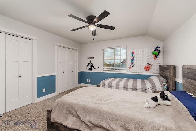 carpeted bedroom featuring multiple closets, vaulted ceiling, and ceiling fan