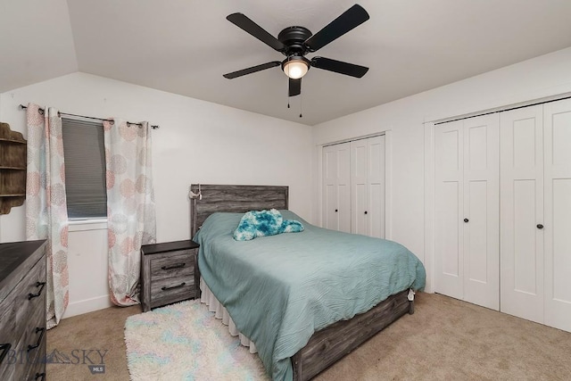 bedroom with vaulted ceiling, two closets, light carpet, and ceiling fan