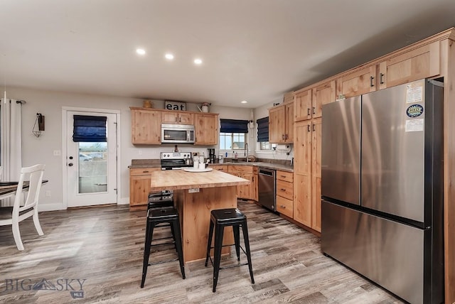 kitchen featuring appliances with stainless steel finishes, butcher block counters, sink, a breakfast bar area, and a center island