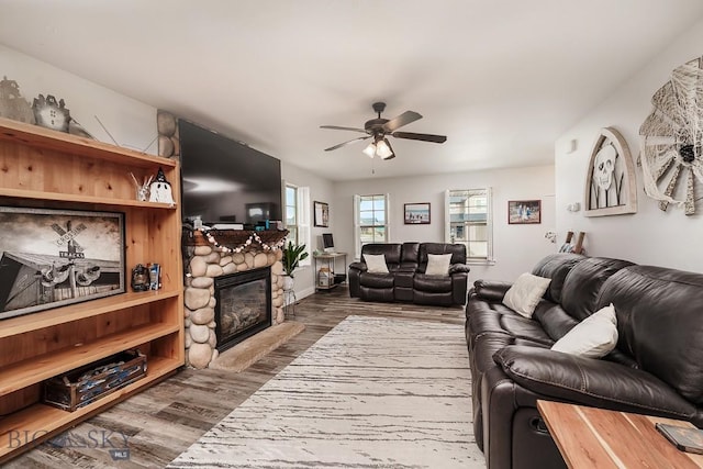 living room with a stone fireplace, dark wood-type flooring, and ceiling fan