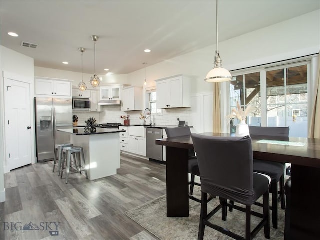 kitchen featuring a kitchen island, white cabinetry, backsplash, hanging light fixtures, and stainless steel appliances