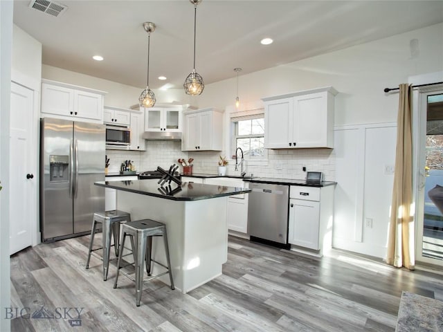 kitchen with stainless steel appliances, a center island, tasteful backsplash, white cabinets, and decorative light fixtures