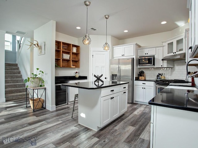 kitchen featuring a kitchen bar, white cabinetry, a center island, hanging light fixtures, and stainless steel appliances