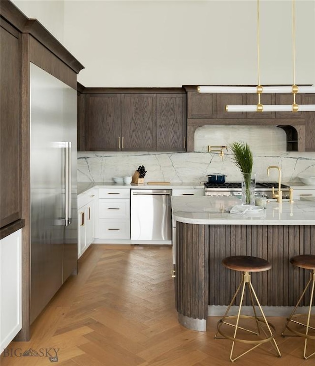 kitchen with stainless steel appliances, backsplash, light parquet floors, a kitchen bar, and white cabinets