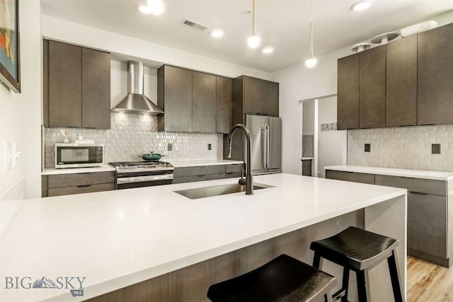 kitchen with pendant lighting, wall chimney range hood, sink, a breakfast bar area, and stainless steel appliances