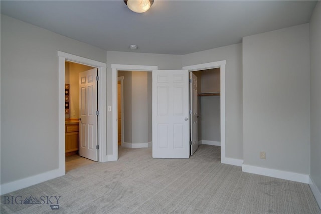 unfurnished bedroom with a walk in closet, ensuite bathroom, a closet, and light colored carpet