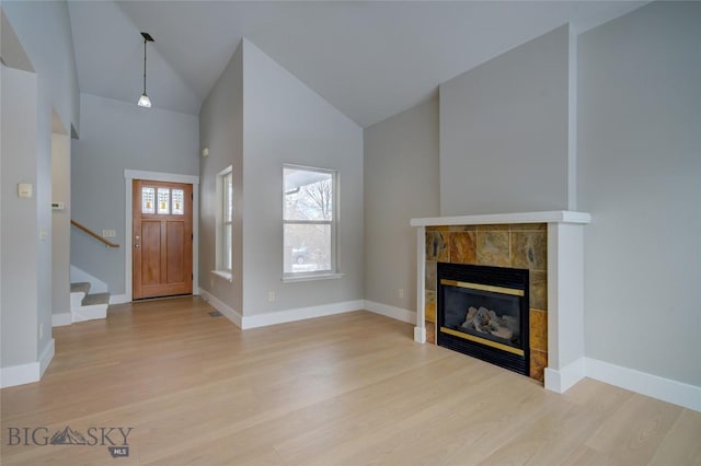 foyer entrance with light hardwood / wood-style floors, high vaulted ceiling, and a tiled fireplace