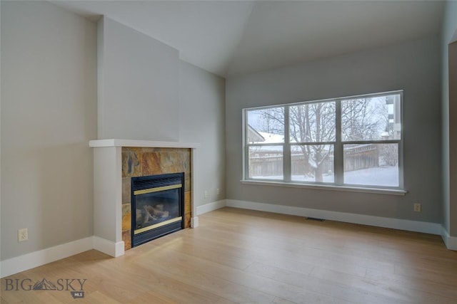 unfurnished living room featuring a tile fireplace, lofted ceiling, and light wood-type flooring