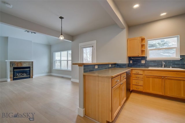 kitchen featuring tasteful backsplash, kitchen peninsula, light hardwood / wood-style floors, decorative light fixtures, and a fireplace