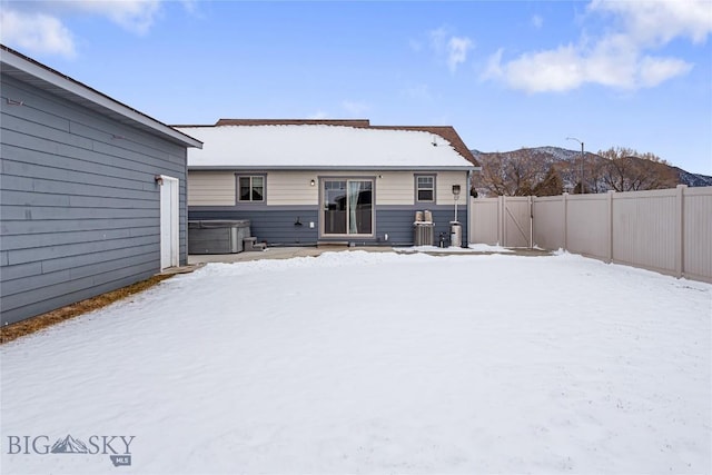 snow covered rear of property featuring a mountain view and a hot tub