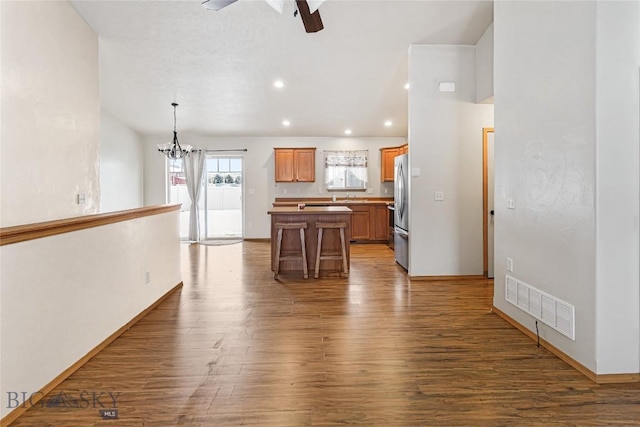 kitchen with a center island, ceiling fan with notable chandelier, stainless steel fridge, decorative light fixtures, and wood-type flooring