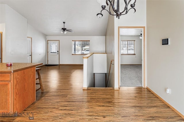 kitchen featuring lofted ceiling, ceiling fan with notable chandelier, hanging light fixtures, dark hardwood / wood-style flooring, and a breakfast bar area