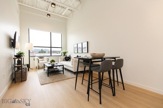 dining area with beamed ceiling, light hardwood / wood-style floors, and a towering ceiling