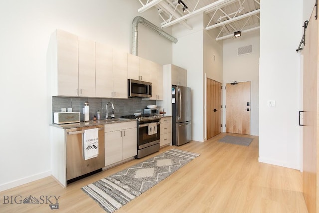 kitchen with a high ceiling, light wood-type flooring, tasteful backsplash, white cabinetry, and stainless steel appliances