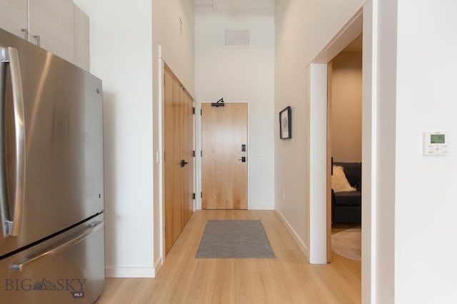 hall with light hardwood / wood-style floors and a towering ceiling