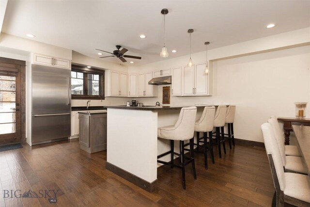 kitchen with a kitchen bar, kitchen peninsula, white cabinets, built in refrigerator, and hanging light fixtures