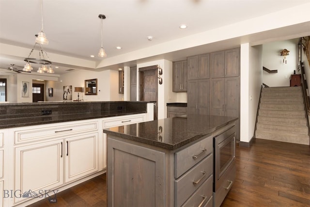 kitchen with stainless steel microwave, a center island, dark hardwood / wood-style floors, dark stone counters, and pendant lighting