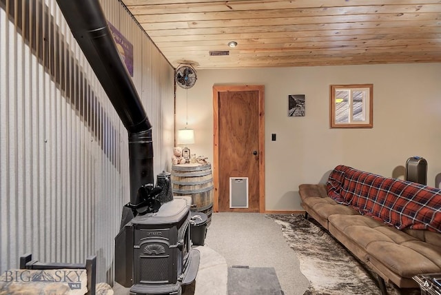 carpeted living room with a wood stove and wood ceiling