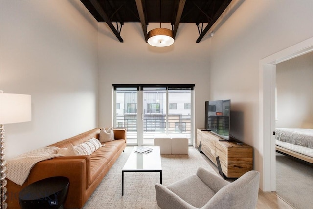 living room with beam ceiling, a high ceiling, and light wood-type flooring