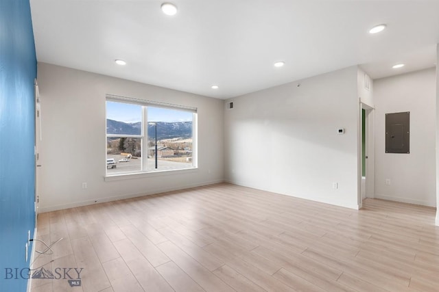 unfurnished room with light wood finished floors, electric panel, baseboards, visible vents, and recessed lighting